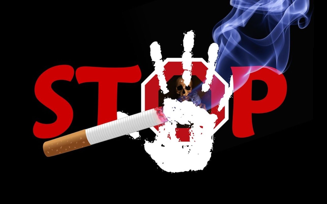 Czerwony napis STOP na czarnym tle. Litera O ma kształt znaku stopu, w jej środku umieszczona została czaszka - symbol śmierci. Napis częściowo przesłania papieros, z którego wydobywa się dym oraz białe odbicie ludzkiej dłoni. 