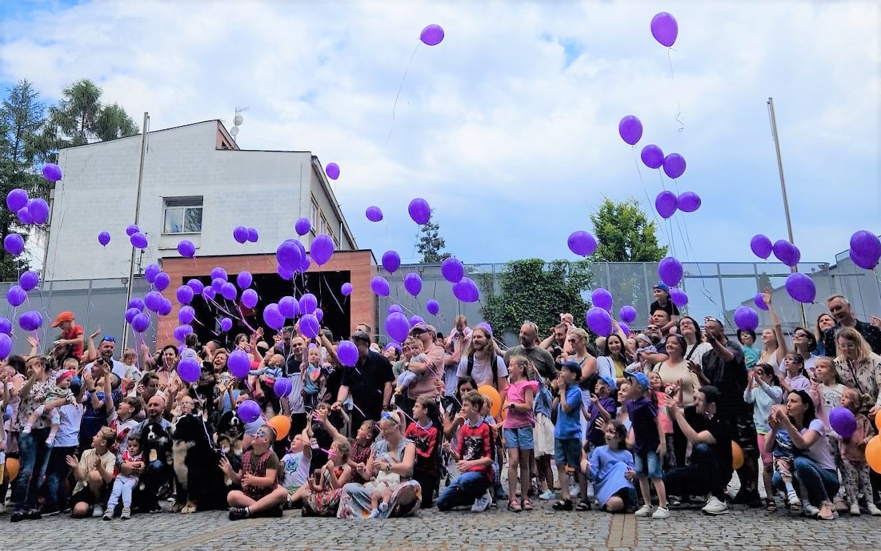 Dzieci urodzone jako wcześniaki wraz z rodzicami trzymają fioletowe balony. Kolor fioletowy symbolizuje wcześniactwo