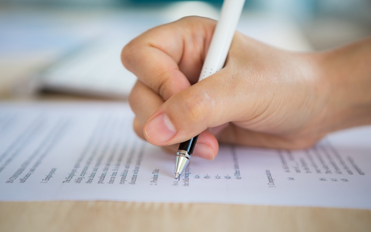 Dłoń trzymająca długopis i wypełniająca formularz ankiety